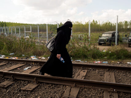 A woman in a long dress is walking on a railroad track
